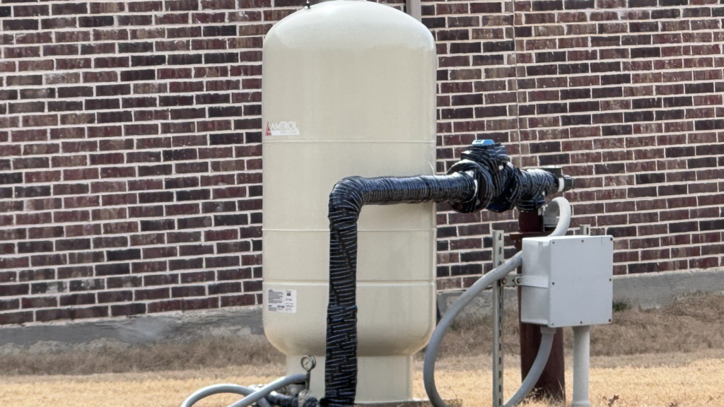 Residential water well pressure tank with insulated exterior piping beside brick home