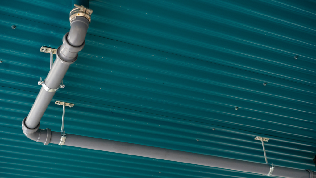 Exterior PVC plumbing installed beneath metal building roof