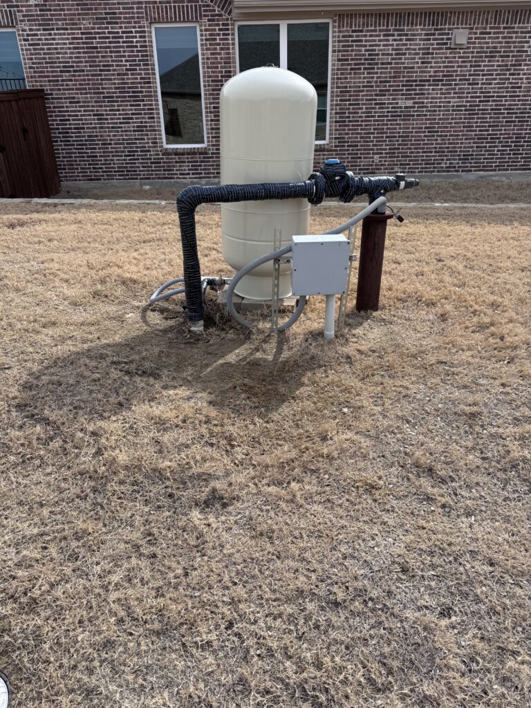 Residential water well pressure tank with insulated exterior piping beside brick home