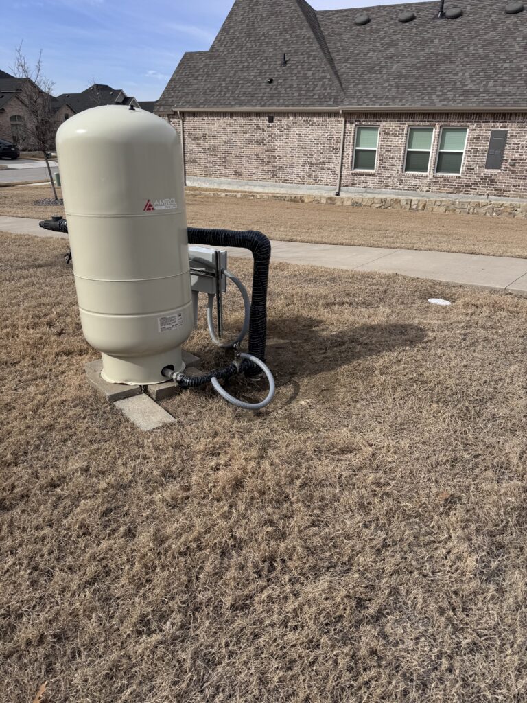 Residential water well pressure tank with insulated exterior piping beside brick home