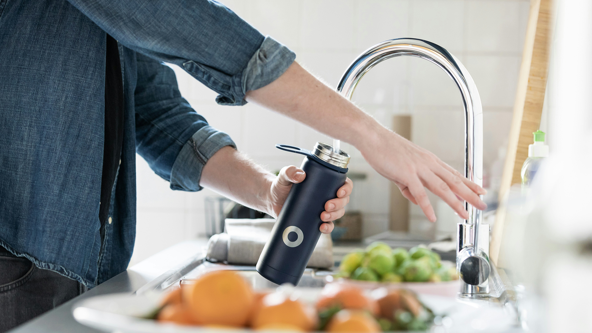 Person filling bottle from kitchen faucet with water filtration device